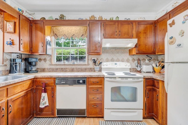 kitchen featuring white appliances, under cabinet range hood, brown cabinets, light countertops, and crown molding
