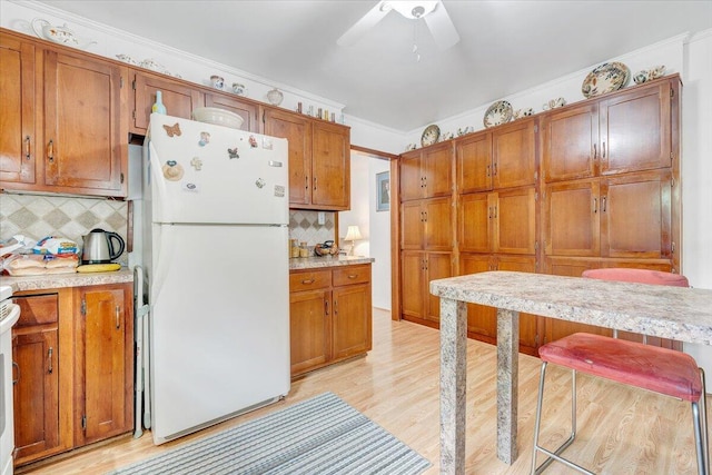 kitchen featuring freestanding refrigerator, brown cabinets, light countertops, decorative backsplash, and ornamental molding