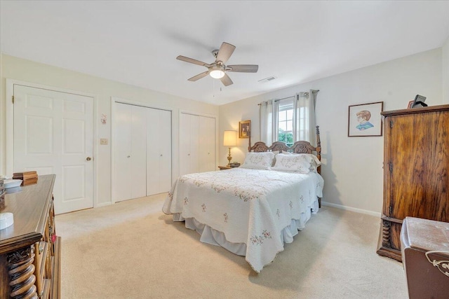 bedroom with two closets, light colored carpet, baseboards, and ceiling fan