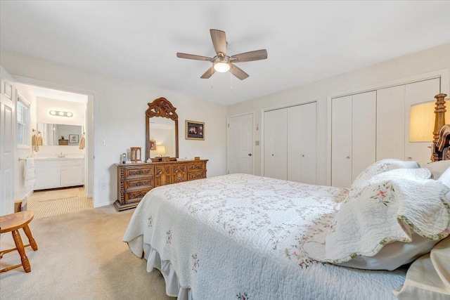 bedroom featuring multiple closets, light colored carpet, connected bathroom, ceiling fan, and a sink