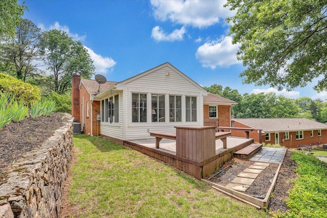 back of property featuring a deck, a chimney, a lawn, and brick siding
