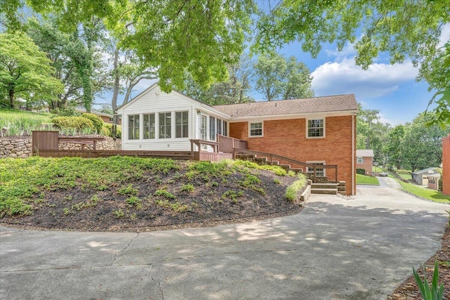 rear view of property with a sunroom, driveway, brick siding, and a deck