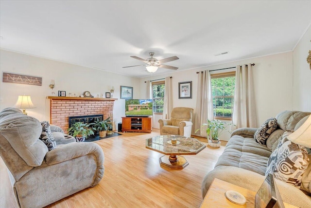 living room featuring wood finished floors, ceiling fan, a brick fireplace, and crown molding