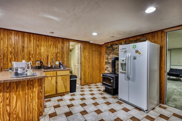 1530 Ridgeview Rd, Floyd, VA 24091 - kitchen featuring white fridge with ice dispenser, wood walls, a wood stove, brown cabinetry, and a textured ceiling