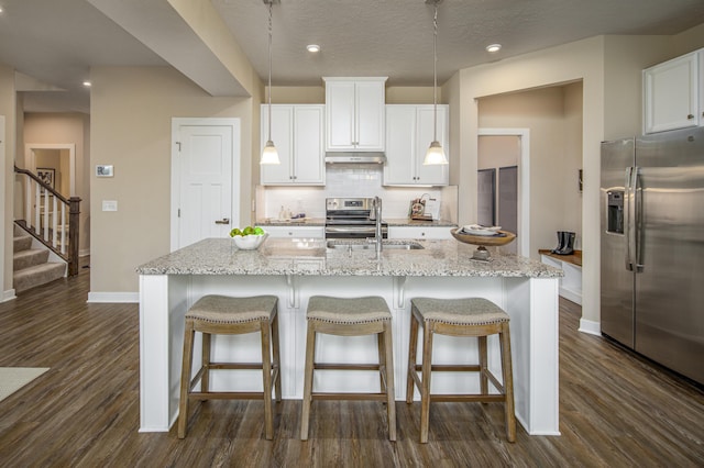 kitchen with stainless steel appliances, under cabinet range hood, baseboards, a sink, and dark wood-style floors