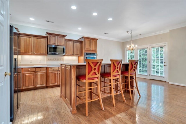 3326 Belshire Ct SW, Roanoke, VA 24014 - kitchen featuring appliances with stainless steel finishes, brown cabinets, a kitchen island, light wood finished floors, and a chandelier