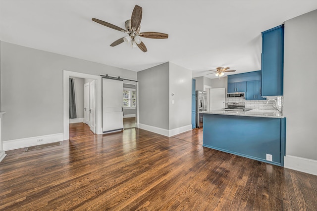 unfurnished living room featuring a ceiling fan, a barn door, dark wood-type flooring, and baseboards