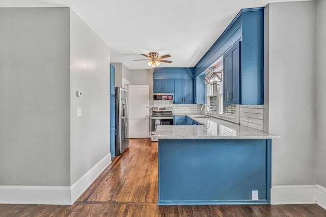 kitchen featuring appliances with stainless steel finishes, a sink, blue cabinetry, tasteful backsplash, and ceiling fan