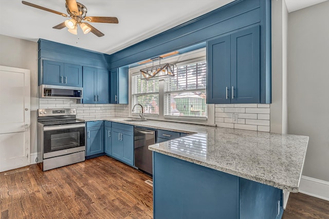 kitchen with appliances with stainless steel finishes, blue cabinetry, a sink, a peninsula, and light stone countertops