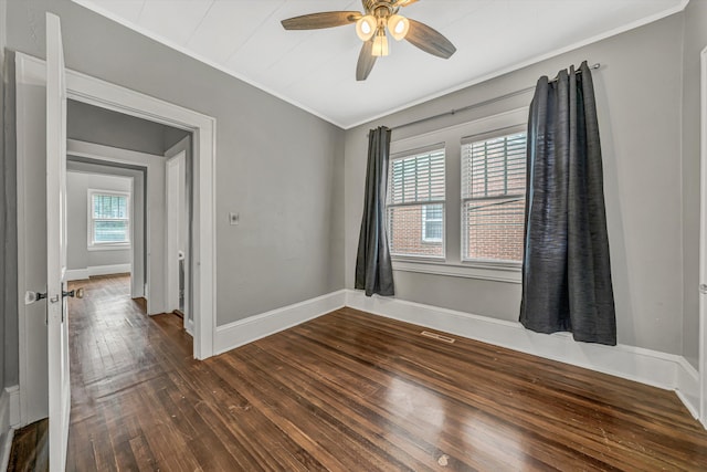 empty room with crown molding, dark wood finished floors, a ceiling fan, and baseboards