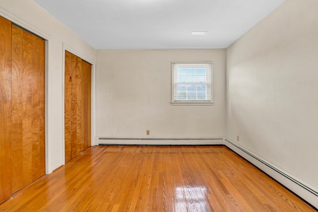 unfurnished bedroom featuring baseboard heating, wood finished floors, and two closets