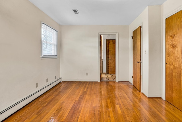 unfurnished bedroom with a baseboard radiator, hardwood / wood-style flooring, and baseboards