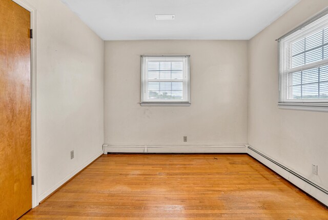 empty room featuring a baseboard heating unit, light wood-type flooring, and baseboards
