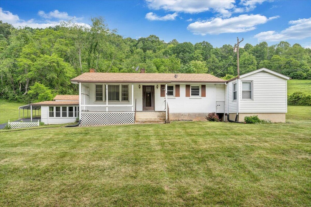 view of front of house featuring a wooded view, a front yard, a chimney, and a porch