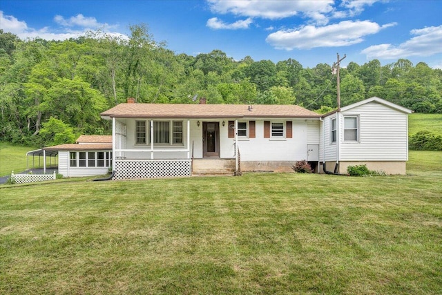 view of front of house featuring a wooded view, a front yard, a chimney, and a porch