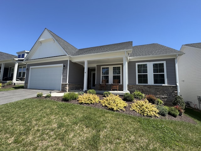 view of front facade featuring covered porch, stone siding, driveway, a garage, and a front lawn