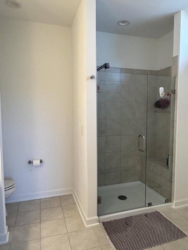 bathroom with tile patterned floors, toilet, a stall shower, and baseboards