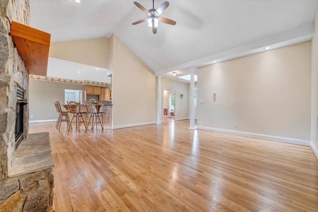 living area with a ceiling fan, a fireplace, light wood-type flooring, high vaulted ceiling, and baseboards
