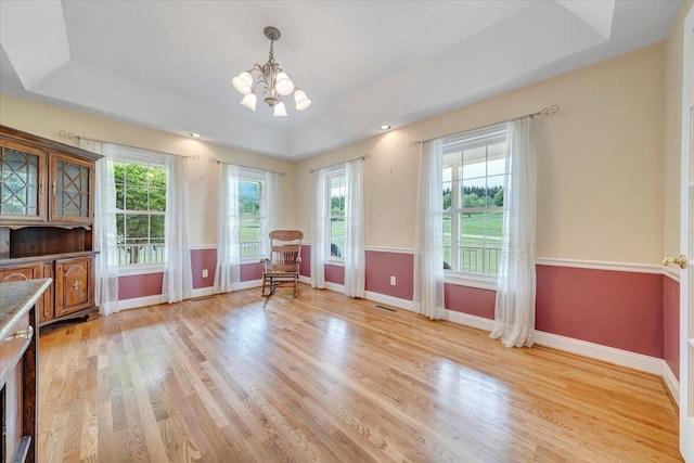 living area featuring a raised ceiling, a chandelier, light wood finished floors, and baseboards