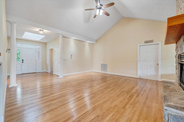 unfurnished living room featuring a ceiling fan, a fireplace, light wood-style flooring, decorative columns, and high vaulted ceiling