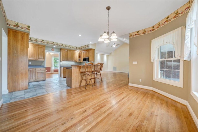 kitchen with a chandelier, a breakfast bar area, light wood finished floors, baseboards, and stainless steel microwave