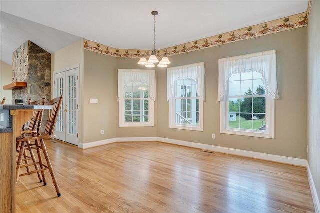 unfurnished dining area featuring wood finished floors, a chandelier, baseboards, and french doors