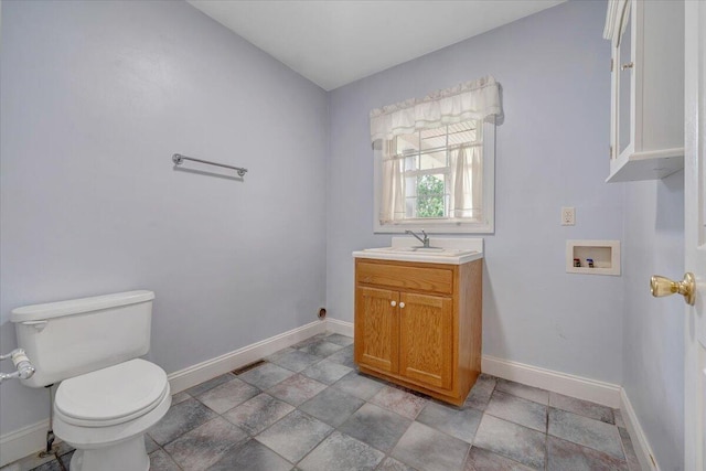 half bathroom with baseboards, toilet, vanity, and stone finish floors