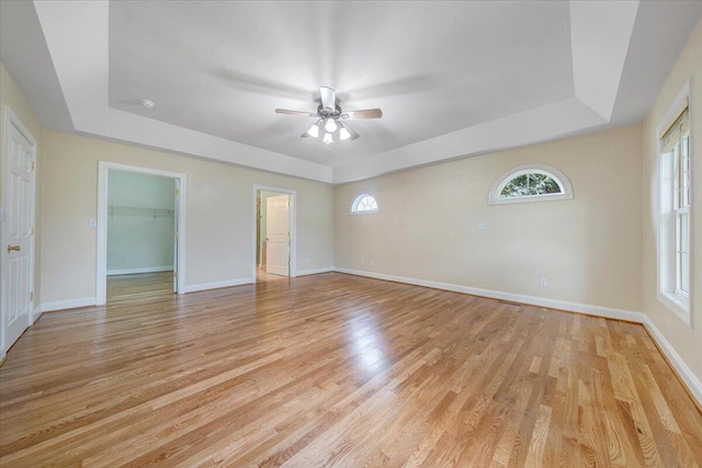 empty room featuring a tray ceiling, ceiling fan, plenty of natural light, and light wood-style flooring