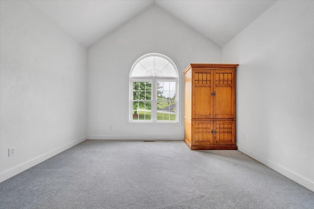 carpeted spare room featuring lofted ceiling and baseboards