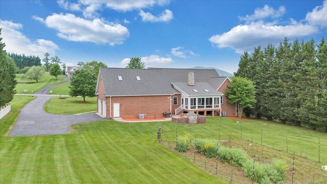back of house featuring driveway, brick siding, a lawn, and a chimney