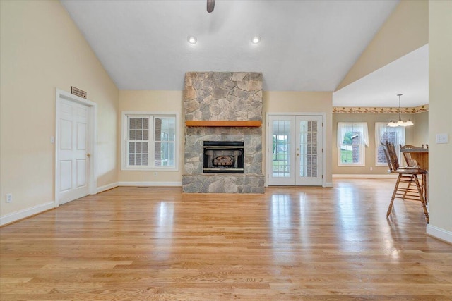 unfurnished living room featuring light wood finished floors, baseboards, a stone fireplace, a chandelier, and high vaulted ceiling
