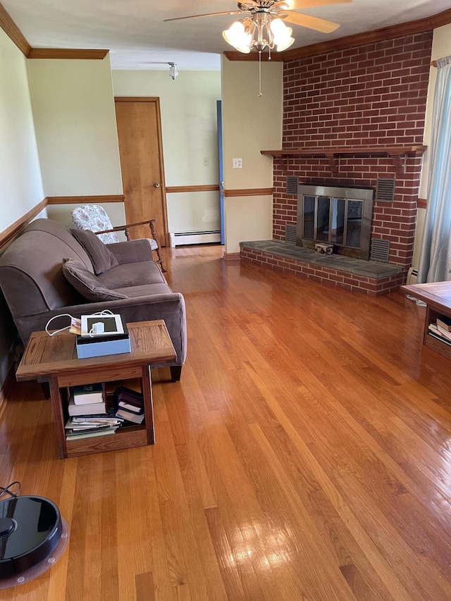 living area featuring a ceiling fan, baseboard heating, wood finished floors, ornamental molding, and a brick fireplace