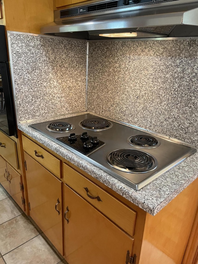 kitchen with stainless steel electric stovetop, under cabinet range hood, light tile patterned floors, and light countertops