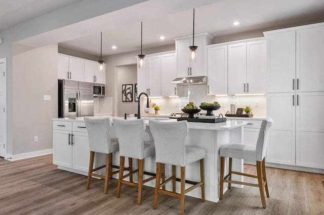 kitchen with stainless steel appliances, under cabinet range hood, light wood-type flooring, a sink, and recessed lighting
