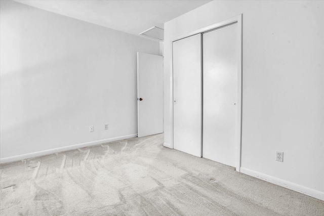 unfurnished bedroom with a closet, carpet, attic access, and baseboards