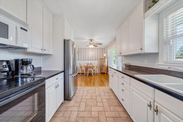 kitchen featuring black electric range oven, white microwave, freestanding refrigerator, and white cabinets