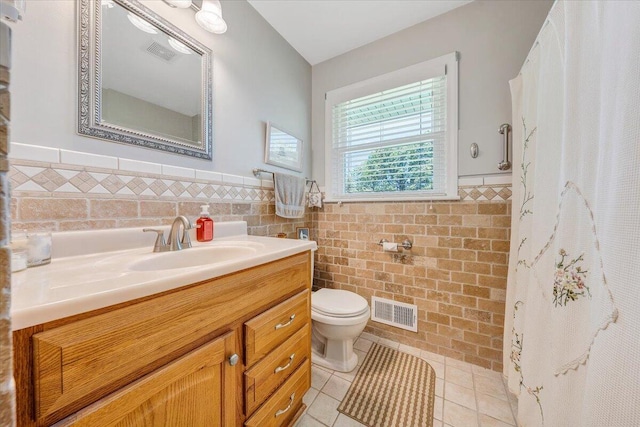 full bathroom with toilet, wainscoting, vanity, tile patterned floors, and tile walls