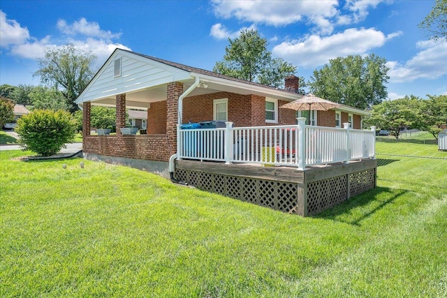 rear view of property with brick siding, a chimney, a yard, and a deck
