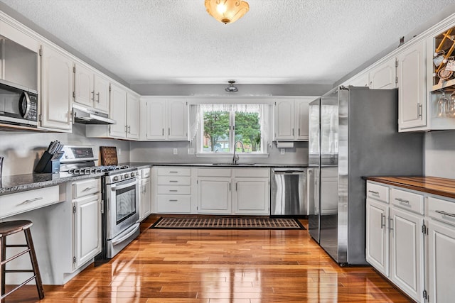 145 W Arrowhead Ct, Troutville, VA 24175 - kitchen with stainless steel appliances, a sink, under cabinet range hood, a textured ceiling, and light wood-type flooring