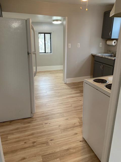 1120 6th St SE, Roanoke, VA 24013 - kitchen with white appliances, under cabinet range hood, light wood finished floors, and baseboards