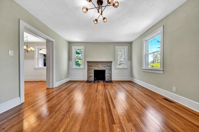 4816 Colonial Ave, Roanoke, VA 24018 - unfurnished living room featuring a chandelier, wood finished floors, a stone fireplace, baseboards, and a textured ceiling