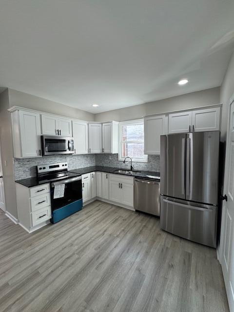 2207 Melrose Ave NW, Roanoke, VA 24017 - kitchen featuring appliances with stainless steel finishes, dark countertops, a sink, decorative backsplash, and light wood-type flooring