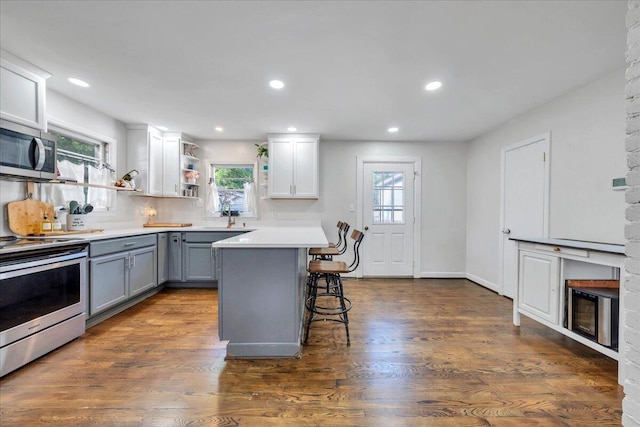 4708 Pawling St NW, Roanoke, VA 24012 - kitchen with gray cabinetry, appliances with stainless steel finishes, a breakfast bar area, light countertops, and dark wood-style flooring