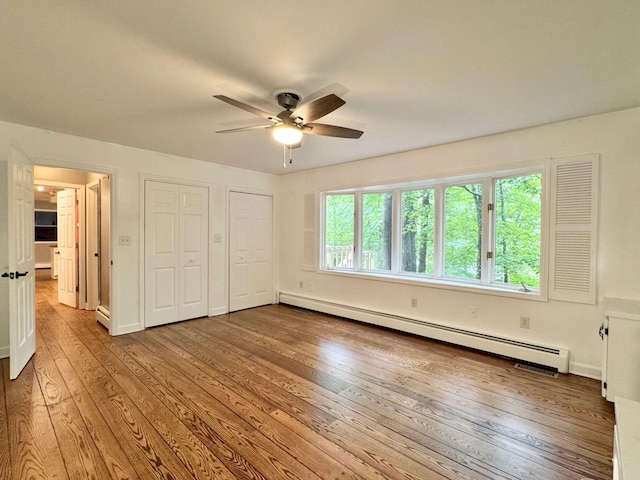 4867 Hunting Hills Dr, Roanoke, VA 24018 - unfurnished bedroom featuring a baseboard radiator, hardwood / wood-style floors, multiple closets, ceiling fan, and baseboards