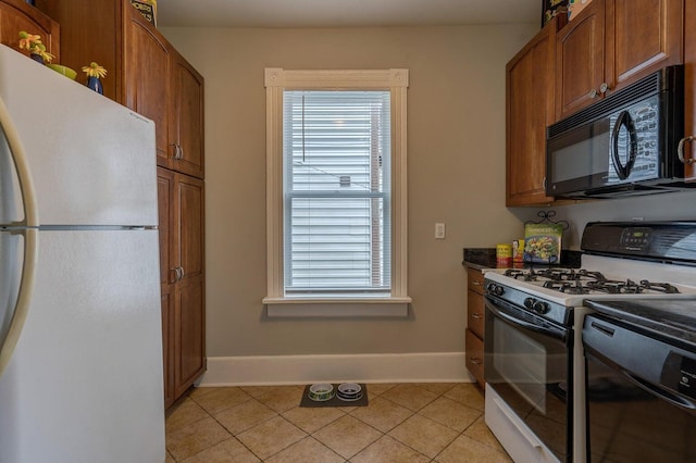 515 Elm Ave SW, Roanoke, VA 24016 - kitchen featuring freestanding refrigerator, black microwave, gas stove, baseboards, and light tile patterned floors