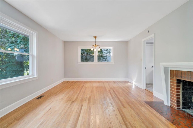 547 Dillard Rd SW, Roanoke, VA 24014 - unfurnished living room with healthy amount of natural light, a chandelier, light wood-style floors, and a brick fireplace
