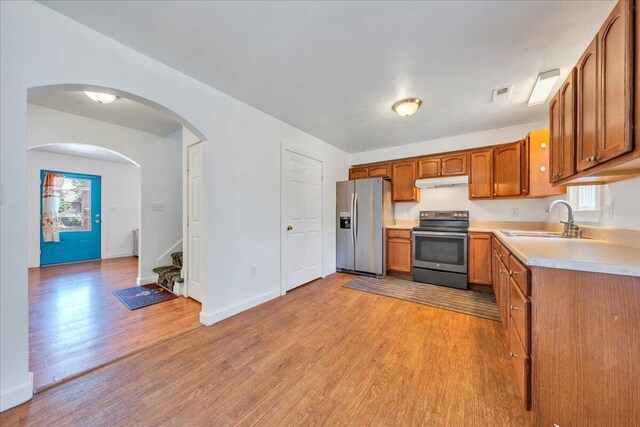 825 Day Ave SW, Roanoke, VA 24016 - kitchen featuring appliances with stainless steel finishes, a sink, under cabinet range hood, brown cabinets, and light wood finished floors