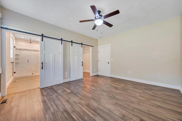 3141 Trinity Rd, Troutville, VA 24175 - unfurnished bedroom featuring a barn door, wood finished floors, a walk in closet, connected bathroom, and ceiling fan