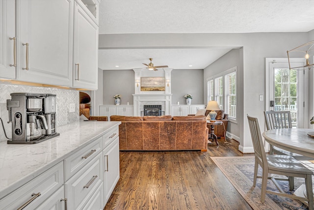 1258 Colby Dr, Forest, VA 24551 - kitchen featuring a glass covered fireplace, ceiling fan, decorative backsplash, dark wood-type flooring, and light stone counters