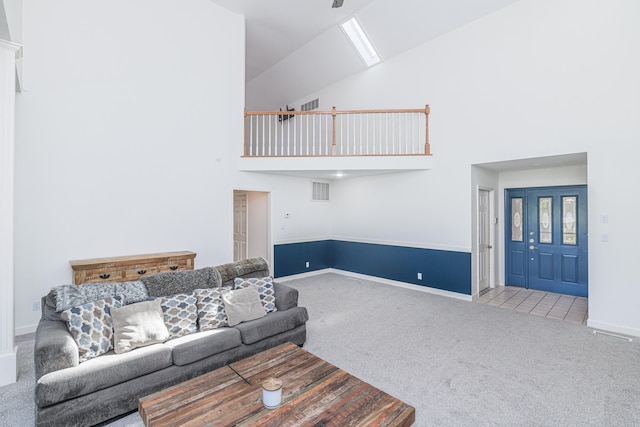 carpeted living room with a towering ceiling, ceiling fan, and a skylight